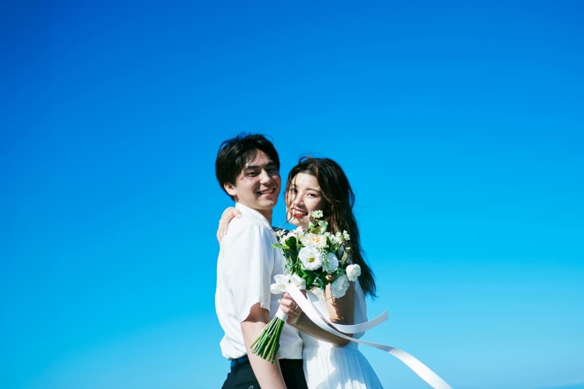 青空の下で寄り添い、微笑むカップル。