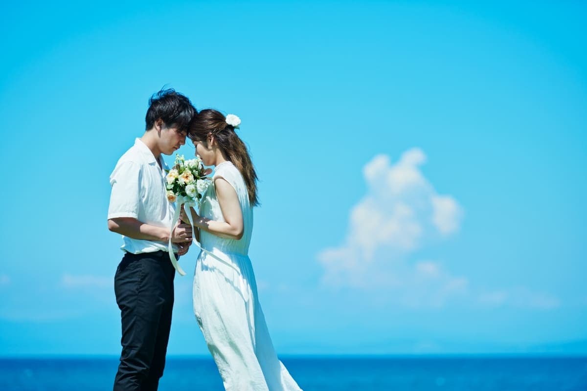 青空と海を背景に、額を寄せ合うカップル。